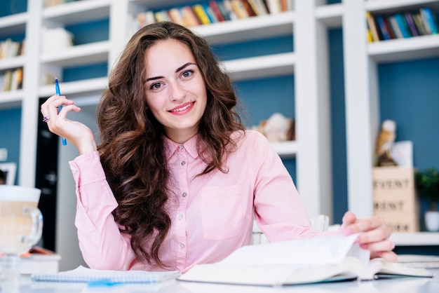 Estudiante con libro y pluma en la biblioteca