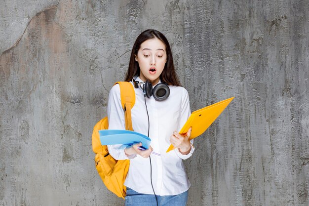 Estudiante con libros de mochila y auriculares en la mano que parece sorprendida. foto de alta calidad