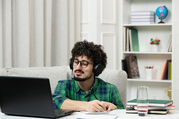 Estudiante en línea chico joven lindo estudiando en la computadora con gafas en camisa verde escuchando una conferencia