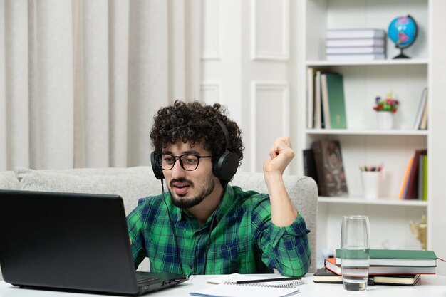 Estudiante en línea chico joven lindo estudiando en la computadora con gafas en camisa verde trabajando duro