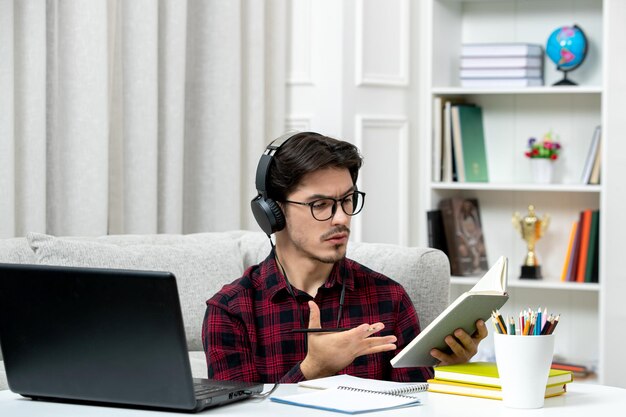 Estudiante en línea chico lindo en camisa a cuadros con gafas estudiando en la computadora confundido sobre la clase