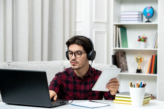 Estudiante en línea chico lindo en camisa a cuadros con gafas estudiando en la computadora escribiendo en el teclado