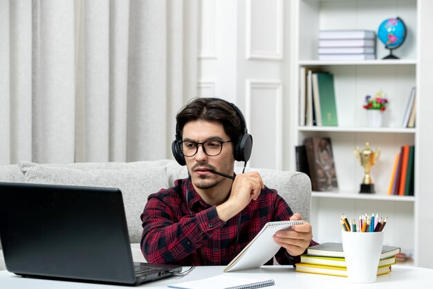 Estudiante en línea chico lindo en camisa a cuadros con gafas estudiando en computadora pensando concentrado