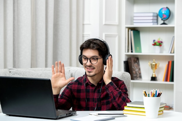 Estudiante en línea joven en camisa a cuadros con gafas estudiando en la computadora agitando las manos