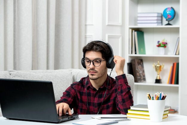 Estudiante en línea joven en camisa a cuadros con gafas estudiando en la computadora escuchando al maestro