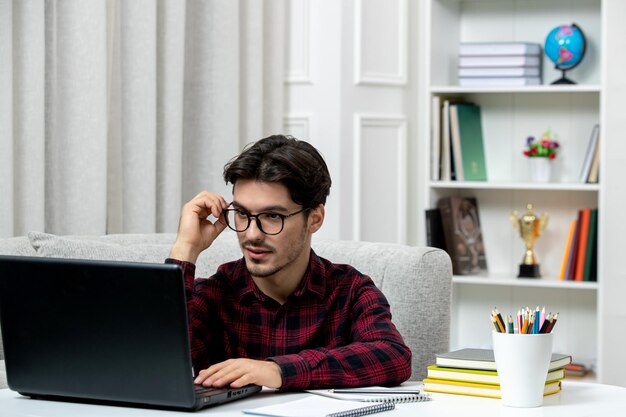 Estudiante en línea joven en camisa a cuadros con gafas estudiando en la computadora escuchando una conferencia