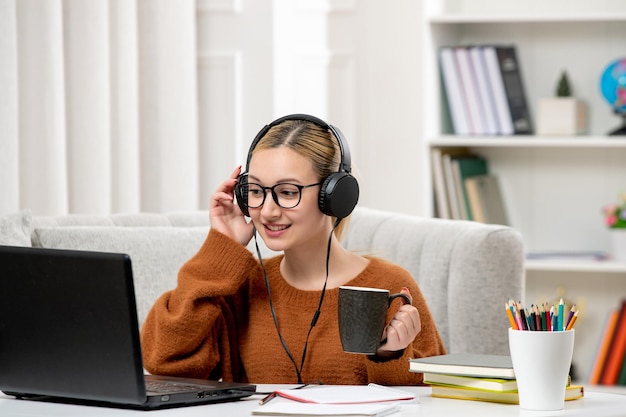 Estudiante en línea linda chica con gafas y suéter estudiando en la computadora escuchando al profesor