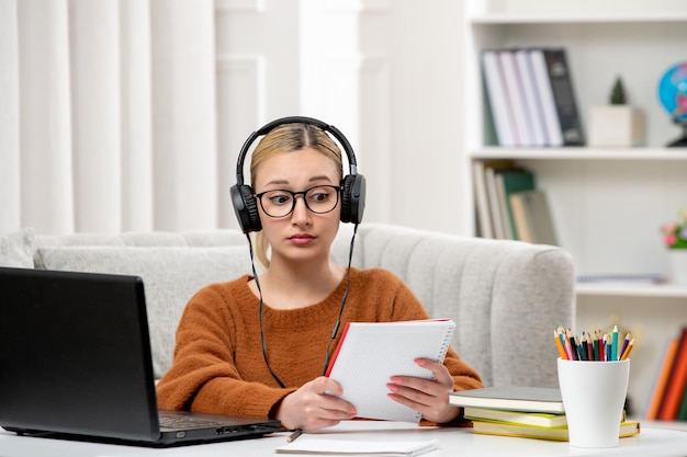 Estudiante en línea linda chica con gafas y suéter estudiando en computadora leyendo notas