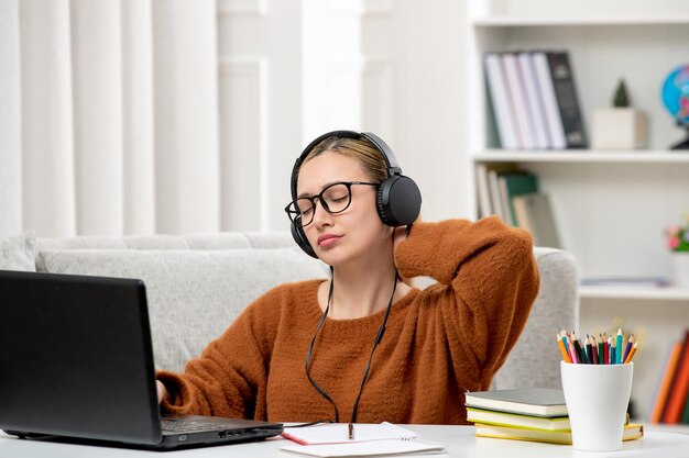 Estudiante en línea linda chica con gafas y suéter estudiando en la computadora tocando el cuello cansado