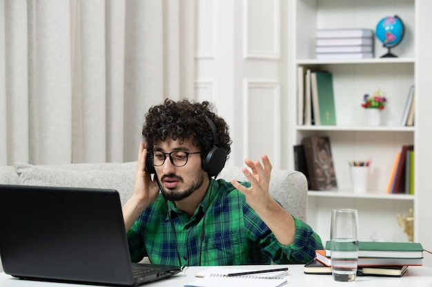 Estudiante en línea lindo joven estudiando en computadora con gafas en camisa verde agitando las manos