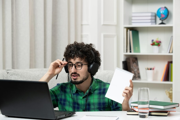 Estudiante en línea lindo joven estudiando en computadora con gafas en camisa verde aprendiendo con pluma