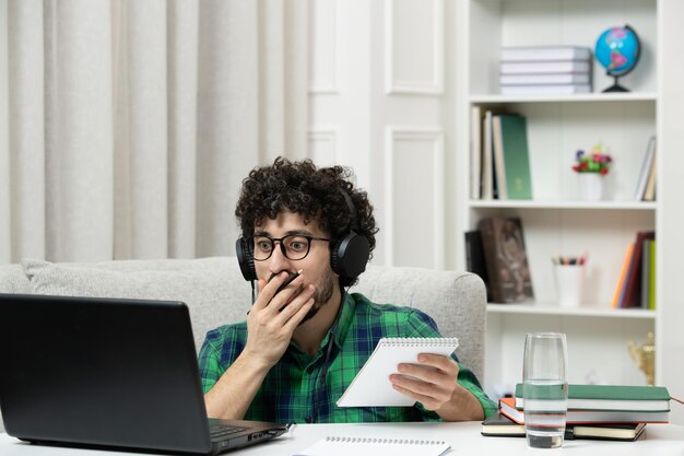 Estudiante en línea lindo joven estudiando en computadora con gafas en camisa verde cubriendo la boca