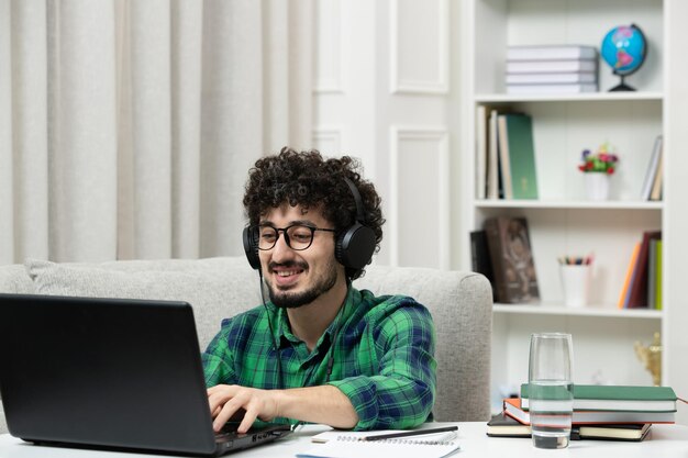 Estudiante en línea lindo joven estudiando en computadora con gafas en camisa verde escribiendo