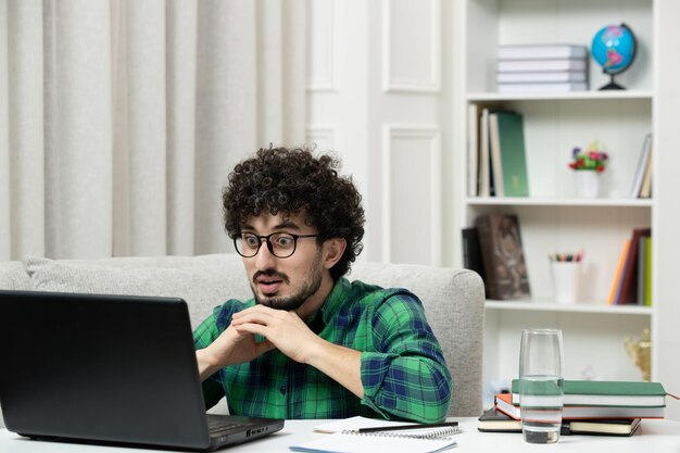Estudiante en línea lindo joven estudiando en la computadora con gafas en camisa verde escuchando al profesor