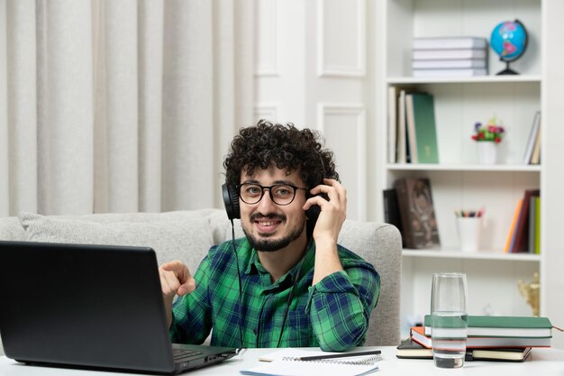 Estudiante en línea lindo joven estudiando en computadora con gafas en camisa verde sonriendo