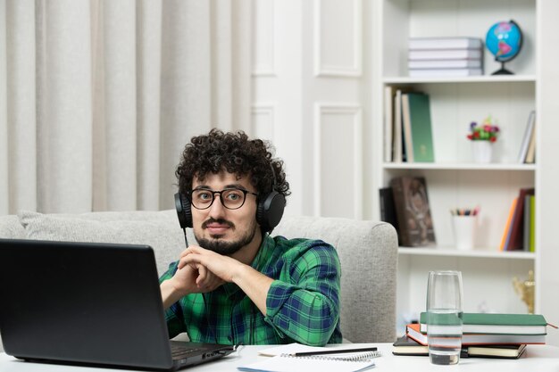 Estudiante en línea lindo joven estudiando en computadora con gafas en camisa verde sonriendo