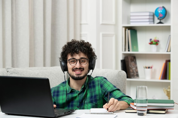 Estudiante en línea lindo joven estudiando en computadora con gafas en camisa verde sonriendo