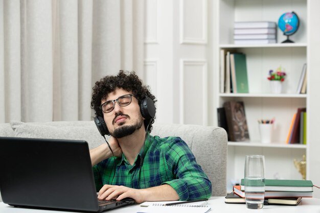 Estudiante en línea lindo joven estudiando en computadora con gafas en camisa verde sosteniendo el cuello