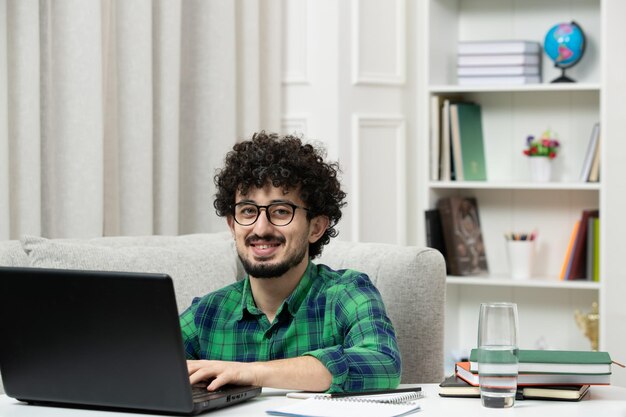 Estudiante en línea lindo joven estudiando en computadora con gafas en camisa verde