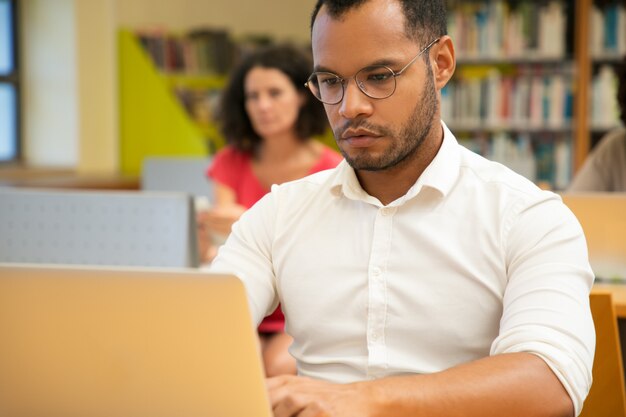 Estudiante masculino adulto enfocado haciendo investigación en biblioteca pública