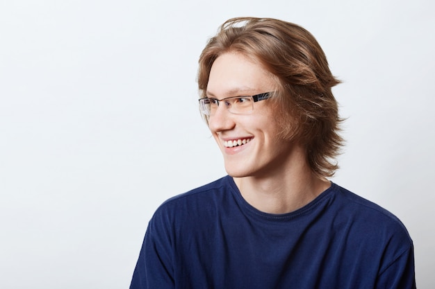 Estudiante masculino con expresión inteligente que tiene buen humor, sonriendo agradablemente mientras se regocija por su éxito en el examen. Empresario masculino sonriente en camiseta casual mirando a un lado con expresión alegre