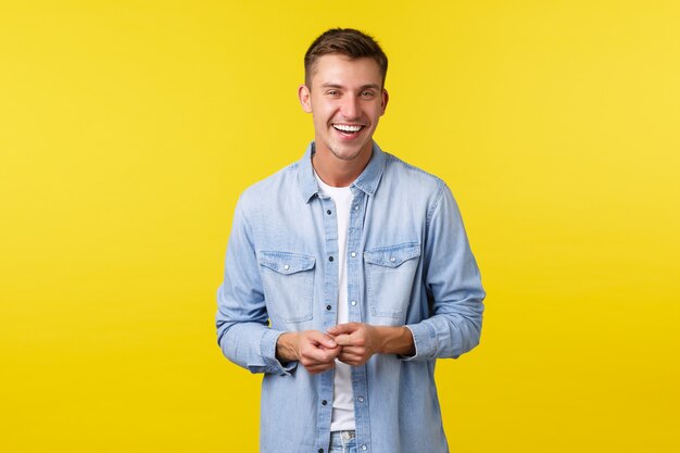 Estudiante masculino feliz hermoso en traje casual, riendo y sonriendo, teniendo una conversación animada. Hombre mirando con alegría la cámara, de pie fondo amarillo, hablando con un amigo.