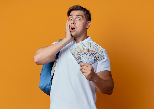 Estudiante masculino hermoso joven sorprendido que lleva el bolso trasero que sostiene el efectivo y que pone la mano