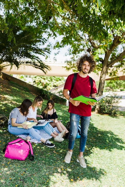 Estudiante masculino con libro parado cerca de amigos