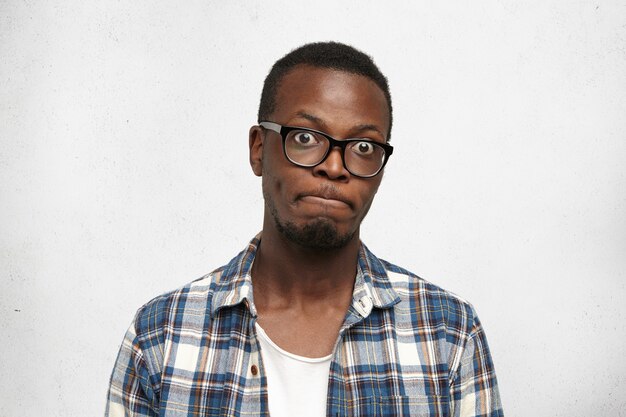 Estudiante masculino de piel oscura de ojos saltones emocionales divertidos con gafas conteniendo la respiración