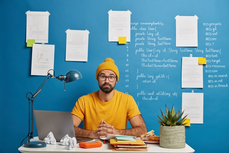 Foto gratuito estudiante masculino sorprendido posa en el escritorio en casa u oficina, usa una computadora portátil para buscar un curso de educación en línea, navega por el sitio web de aprendizaje a distancia