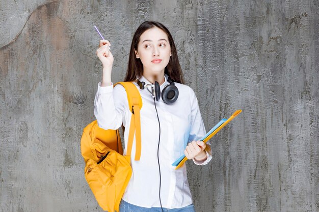 Estudiante con mochila amarilla y auriculares de pie con libro. foto de alta calidad