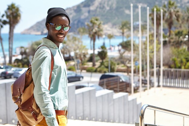 Estudiante de moda con sombrero y sombras disfrutando de un clima cálido y soleado