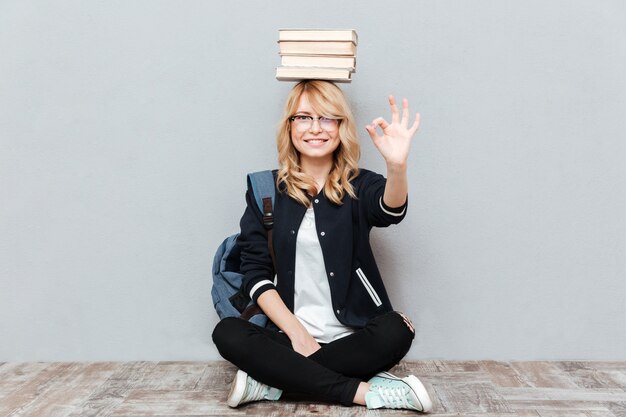 Estudiante de mujer joven alegre que sostiene los libros en la cabeza.