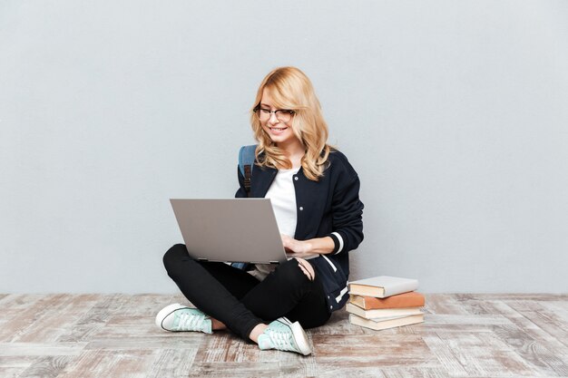 Estudiante de mujer joven alegre que usa la computadora portátil.