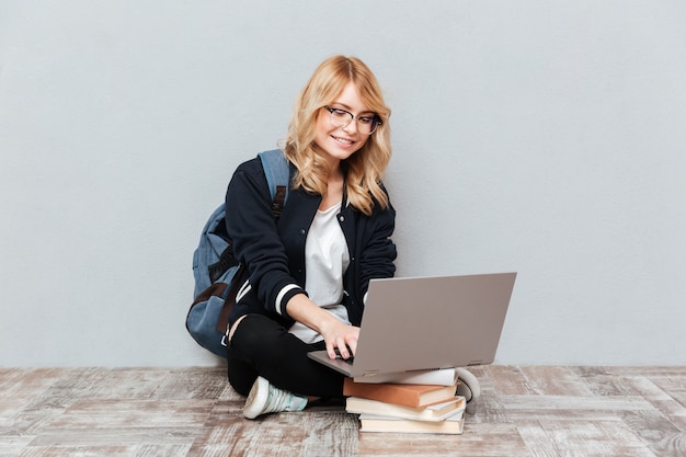 Estudiante de mujer joven alegre que usa la computadora portátil.