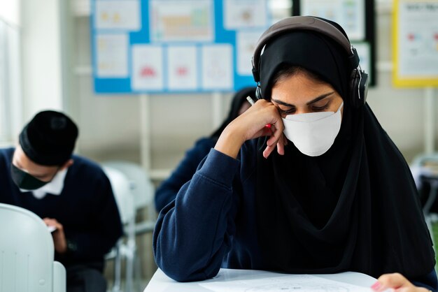Estudiante musulmán con máscara estudiando en un aula