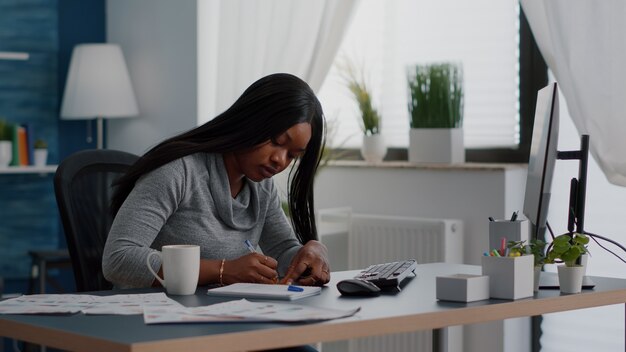 Estudiante negro escribiendo ideas de educación en notas stickey sentado en la mesa de escritorio en la sala de estar