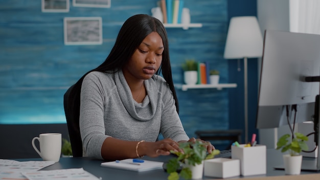 Estudiante negro sentado en el escritorio escribiendo la tarea escolar en el cuaderno durante la educación de cursos en línea