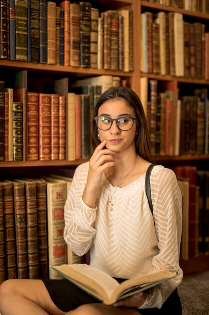 Estudiante pensativo que se sienta con el libro en biblioteca