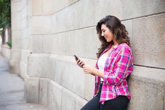 Estudiante positivo apoyado en la pared y el uso de teléfono