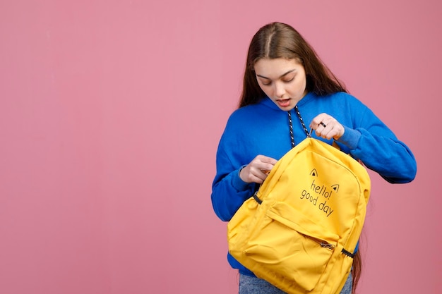 Una estudiante preocupada y emocionada con ropa informal buscando algo en una mochila amarilla