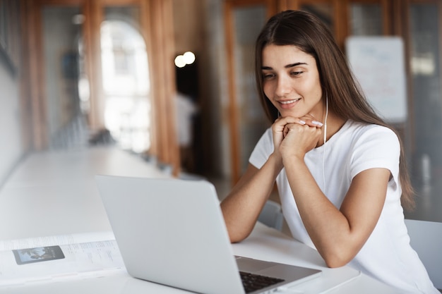 Estudiante que usa una computadora portátil para llamar a los padres en el extranjero. Mujer joven con un cuaderno para escuchar y ver una película.