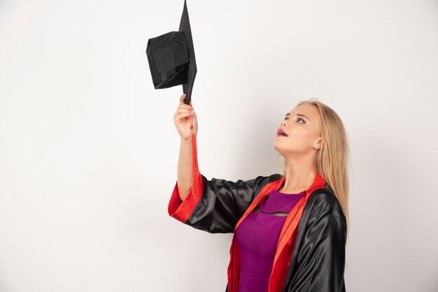 Estudiante rubia mirando su gorra en blanco.