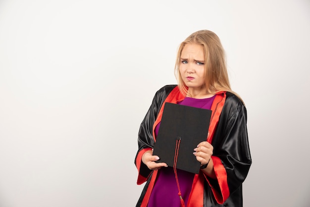 Estudiante rubia sosteniendo su gorra en blanco.