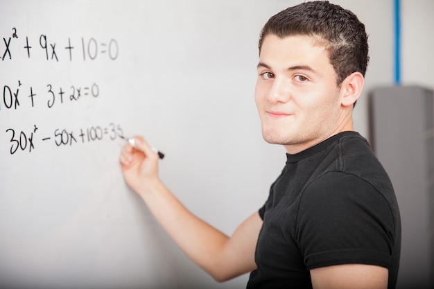 Foto gratuita estudiante de secundaria hispano masculino resolviendo algunos problemas matemáticos en una pizarra blanca en la escuela