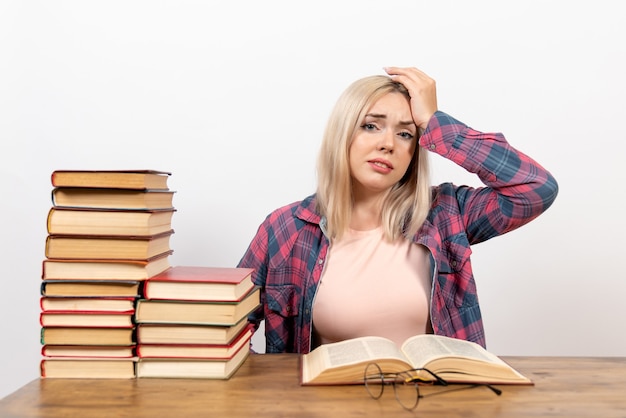 Estudiante sentada con libros y leyendo posando en blanco