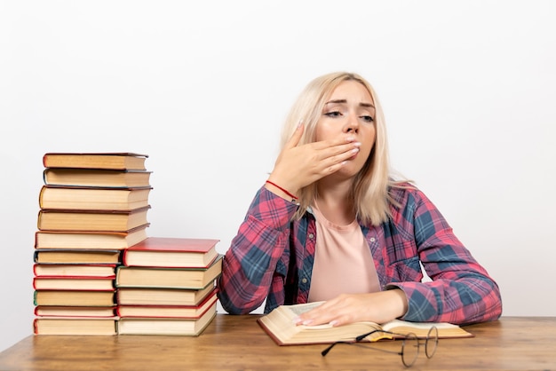 Estudiante sentada con libros sintiéndose cansada y bostezando en blanco