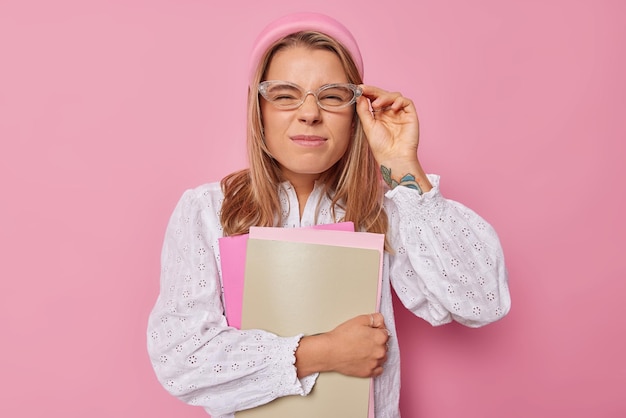 Una estudiante seria mira a través de espectáculos transparentes vestidos con poses de blusa blanca con cuadernos en el interior que van a tener clases en la universidad aisladas sobre fondo rosa. concepto de estudio