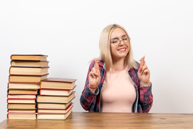 Estudiante solo sentada con libros cruzando los dedos sobre blanco