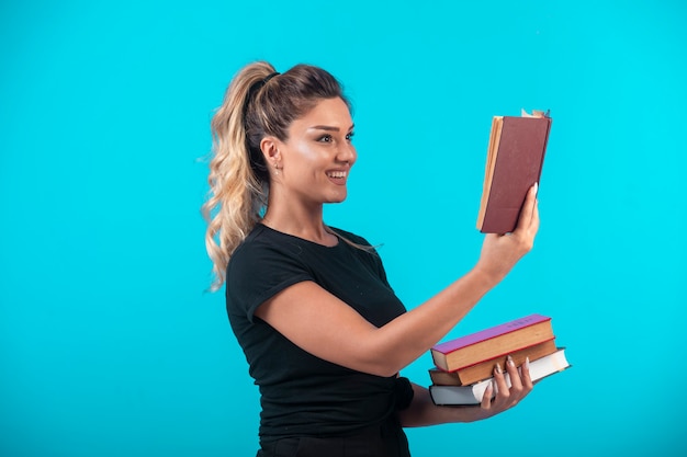 Estudiante sosteniendo una gran cantidad de libros y leyendo uno de ellos.